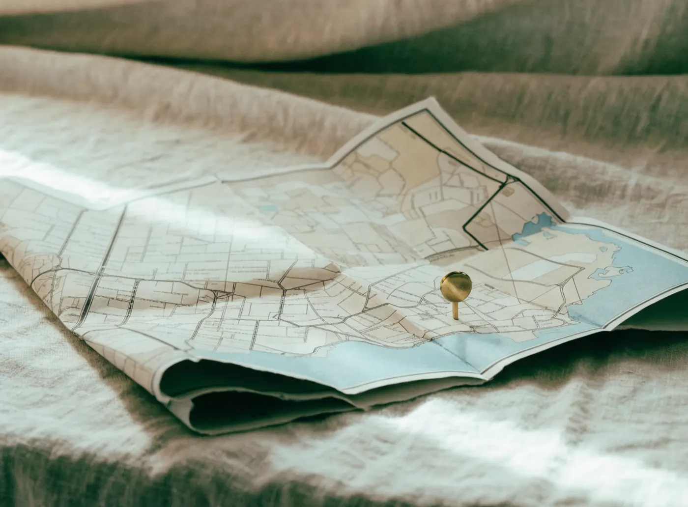 Plan de ville en papier avec une punaise dorée, posé sur du lin