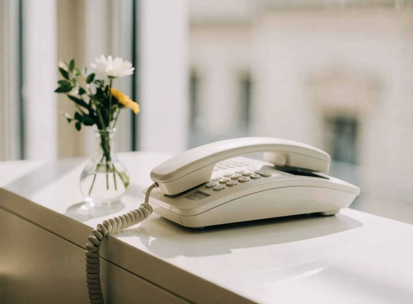 Téléphone blanc et petit bouquet de fleurs sur un comptoir d’accueil lumineux