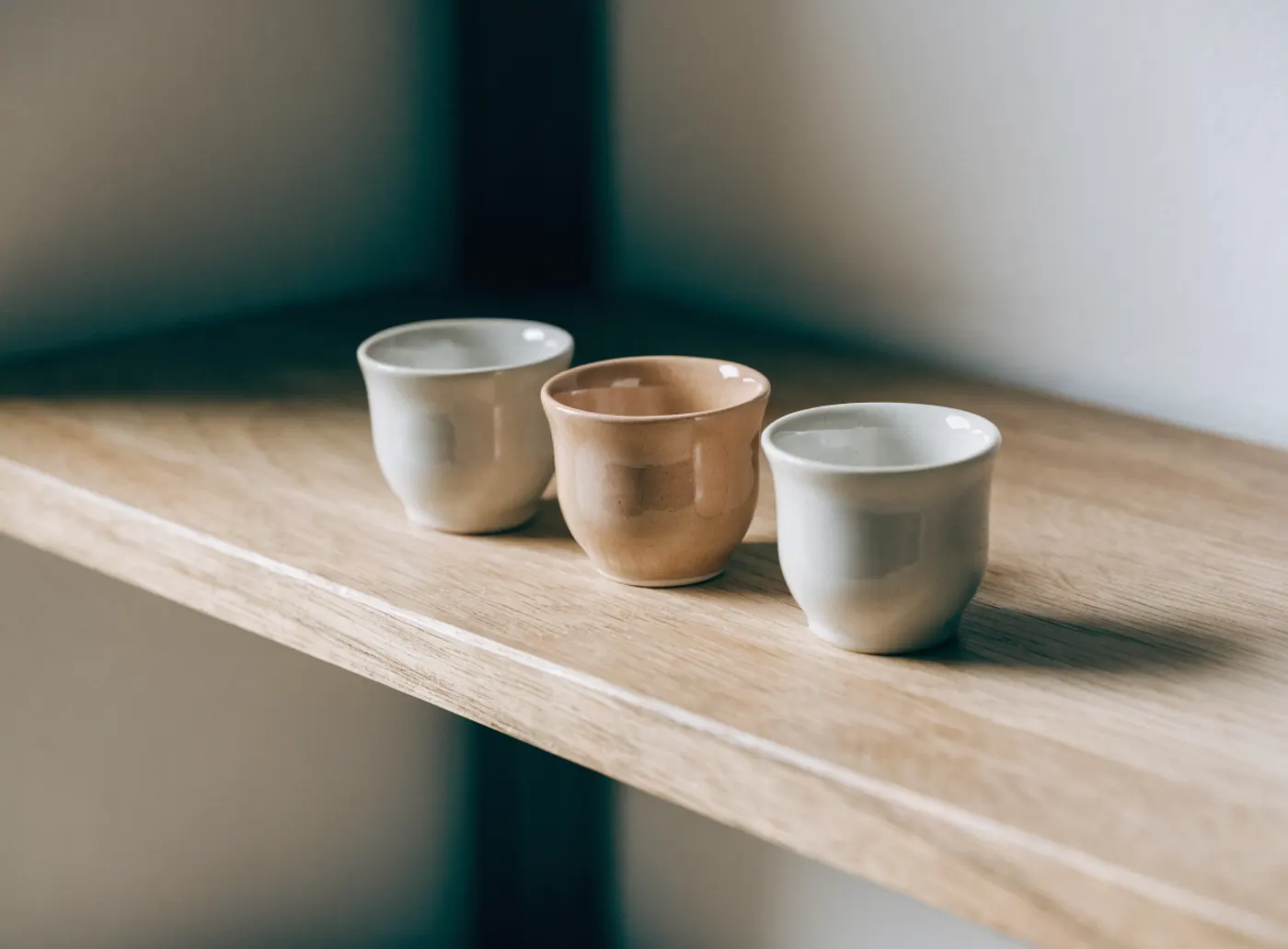 Trois petites tasses sur une tablette, celle du milieu d’une autre couleur