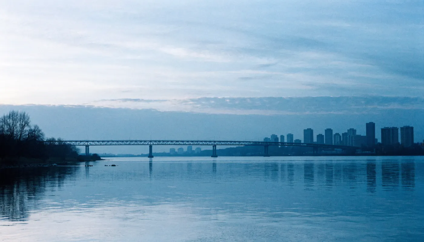 Pont enjambant la rivière à l’aube, silhouette de la ville au loin